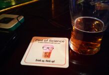 Um copo de cerveja quase vazio com uma base para copos da Pint of Science