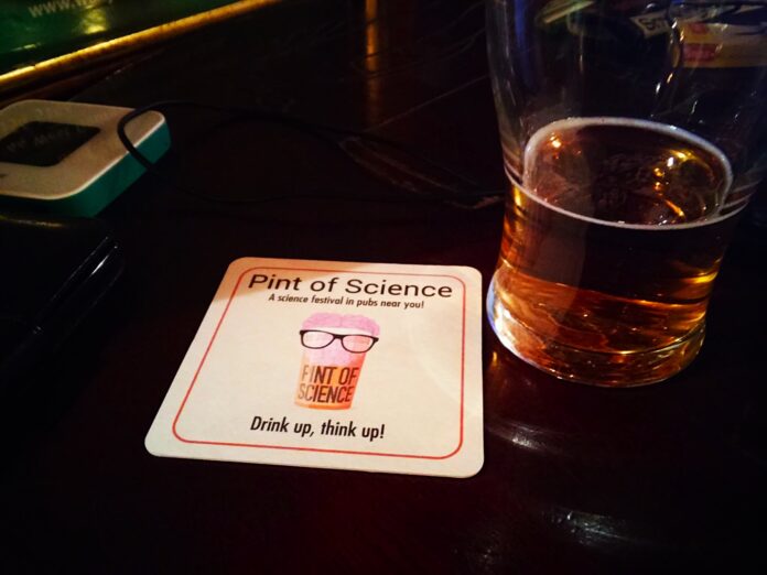 Um copo de cerveja quase vazio com uma base para copos da Pint of Science
